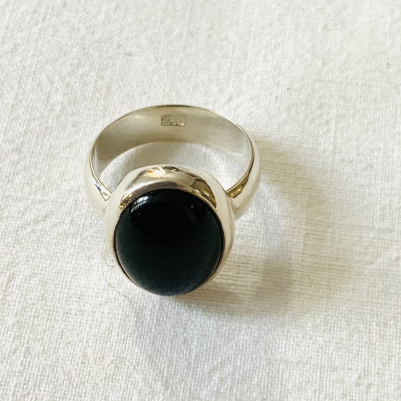 Op de afbeelding: Een zilveren ring met een zwarte ovale edelsteen. De ring is gezet in een eenvoudige bezel setting.