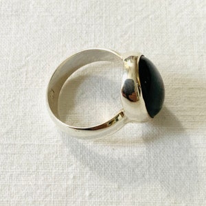 Op de afbeelding: Een zilveren ring met een zwarte ovale edelsteen. De ring is gezet in een gladde, ronde band.