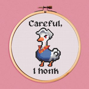 May include: A white cross-stitch embroidery hoop with a white background and a cartoon goose with a red bandana and blue shirt. The text "Careful, 1 honk" is stitched in black thread.