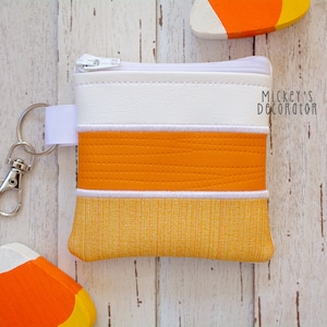 May include: A small white zippered pouch with a key chain. The pouch has three stripes of orange and white fabric. The text "Mickey's Decorator" is printed on the pouch.