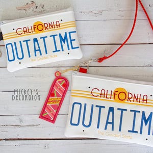May include: White zippered pouches and a keychain featuring a California license plate design with the text "OUTATIME" in blue. The pouches have a red strap and a keychain with a pink and red design.
