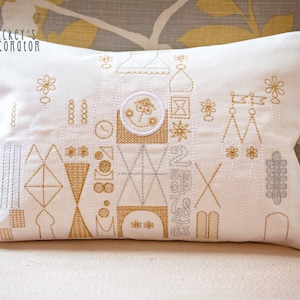 May include: White pillow with gold and silver embroidery depicting a castle with a clock face. The pillow has the text "Mickey's Decorator" in the top left corner.