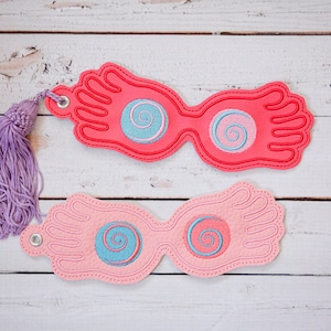 Peut inclure: Deux paires de lunettes de style Harry Potter en feutre rose et rouge avec un pompon violet. Les lunettes ont un motif en spirale dans les verres.
