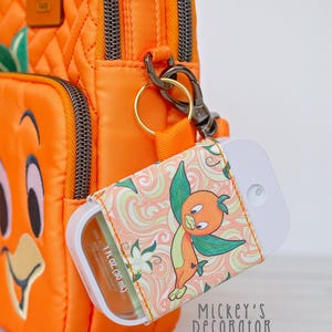 Puede incluir: Bolso bandolera naranja con una funda a juego con el dise&ntilde;o de Orange Bird. La funda, que contiene un pulverizador blanco, est&aacute; sujeta al bolso con un cierre dorado. El bolso tiene un patr&oacute;n acolchado y cierre de cremallera.
