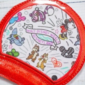 May include: Red glitter fabric ear headband with a clear plastic dome featuring a white fabric patch with a black and white print of various Disney characters and the text "Walt Disney World Disneyland".