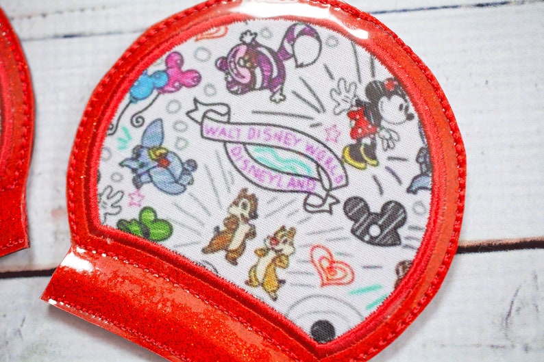 May include: Red glitter fabric ear headband with a clear plastic dome featuring a white fabric patch with a black and white print of various Disney characters and the text "Walt Disney World Disneyland".