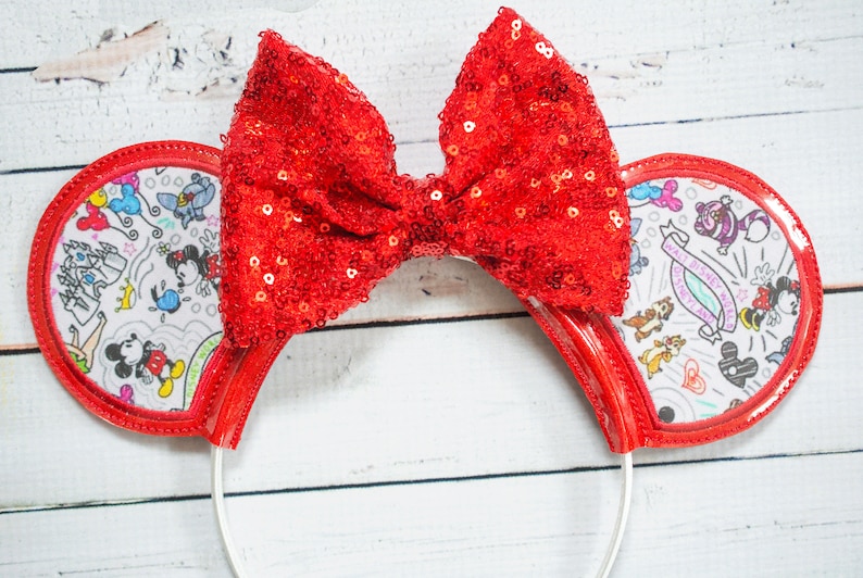 May include: Red sequin bow headband with white ears featuring a black and white doodle design of Mickey Mouse characters and the text "Walt Disney World".