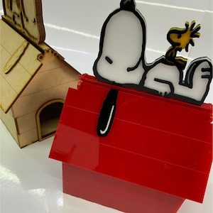 May include: A red doghouse with a white and black Snoopy figure and a yellow Woodstock figure on top. A wooden doghouse is in the background. Vector file icons are at the bottom.