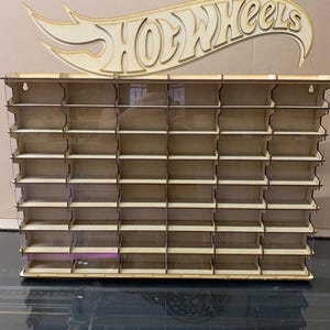 May include: Wooden Hot Wheels display stand with clear acrylic shelves. The stand has 48 slots for displaying Hot Wheels cars. The stand is made of natural wood and has a Hot Wheels logo on top.