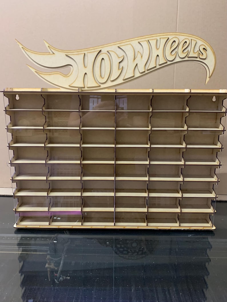May include: Wooden Hot Wheels display stand with clear acrylic shelves. The stand has 48 slots for displaying Hot Wheels cars. The stand is made of natural wood and has a Hot Wheels logo on top.