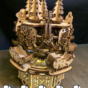 May include: A wooden Christmas carousel with laser-cut details. The carousel features miniature sleighs, Christmas trees, and snowflake designs. Santa Claus and bell illustrations are also present. The base has decorative cutouts, and the overall design is in shades of brown and tan.