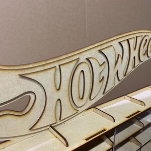 May include: A wooden Hot Wheels display stand with a cutout of the Hot Wheels logo. The stand has multiple shelves for storing toy cars.