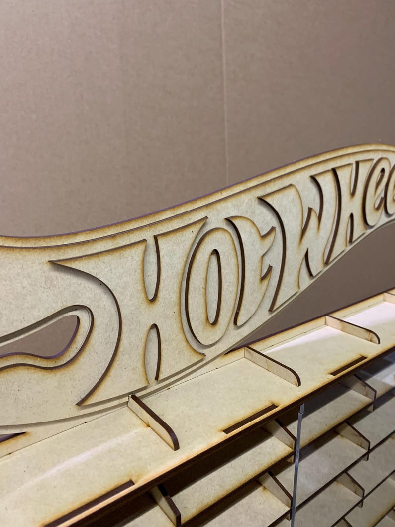 May include: A wooden Hot Wheels display stand with a cutout of the Hot Wheels logo. The stand has multiple shelves for storing toy cars.