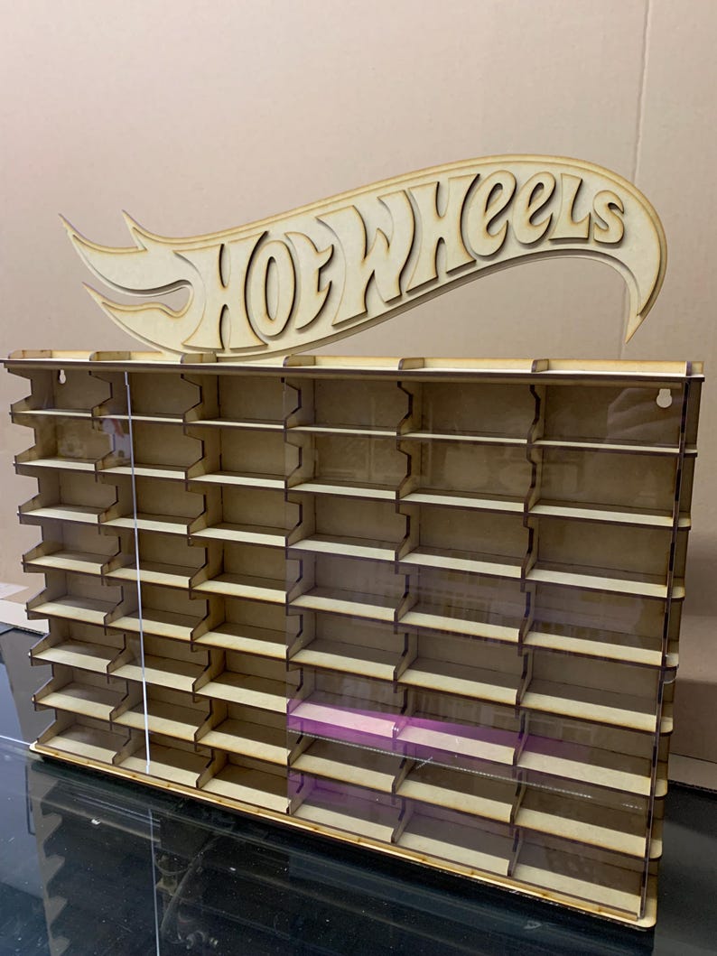 May include: Wooden Hot Wheels display shelf with a cutout Hot Wheels logo. The shelf has 48 slots for displaying Hot Wheels cars. The shelf is made of wood and has a clear acrylic front.
