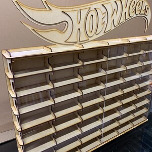 May include: A wooden Hot Wheels display shelf with clear acrylic panels. The shelf has 24 slots for storing Hot Wheels cars. The shelf is topped with a wooden Hot Wheels logo.