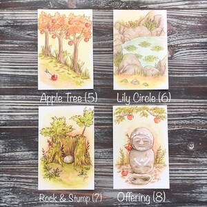 Op de afbeelding: Vier aquarel illustraties op witte kaarten. Linksboven appelbomen met rode appels en de tekst "Apple Tree (5)". Rechtsboven een vijver met waterlelies en de tekst "Lily Circle (6)". Linksonder een rots en een stronk met de tekst "Rock & Stump (7)". Rechtsonder een stenen beeld met de tekst "Offering (8)".