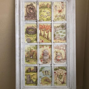 Op de afbeelding: Een wit omkaderd kunstwerk met twaalf kleine, ge&iuml;llustreerde sc&egrave;nes. De sc&egrave;nes tonen grillige landschappen met bomen, rotsen en figuren. Het kunstwerk heeft een verweerde, vintage uitstraling, met een wit geschilderde lijst. De illustraties zijn in zachte, aardse tinten.