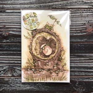 Op de afbeelding: Een pakket van 12 wenskaarten met een aquarel illustratie van een boomstronk en een wezen. De kaarten zitten in een doorzichtige plastic hoes. Het pakket heeft een ronde sticker met de tekst "Korok Puzzles".