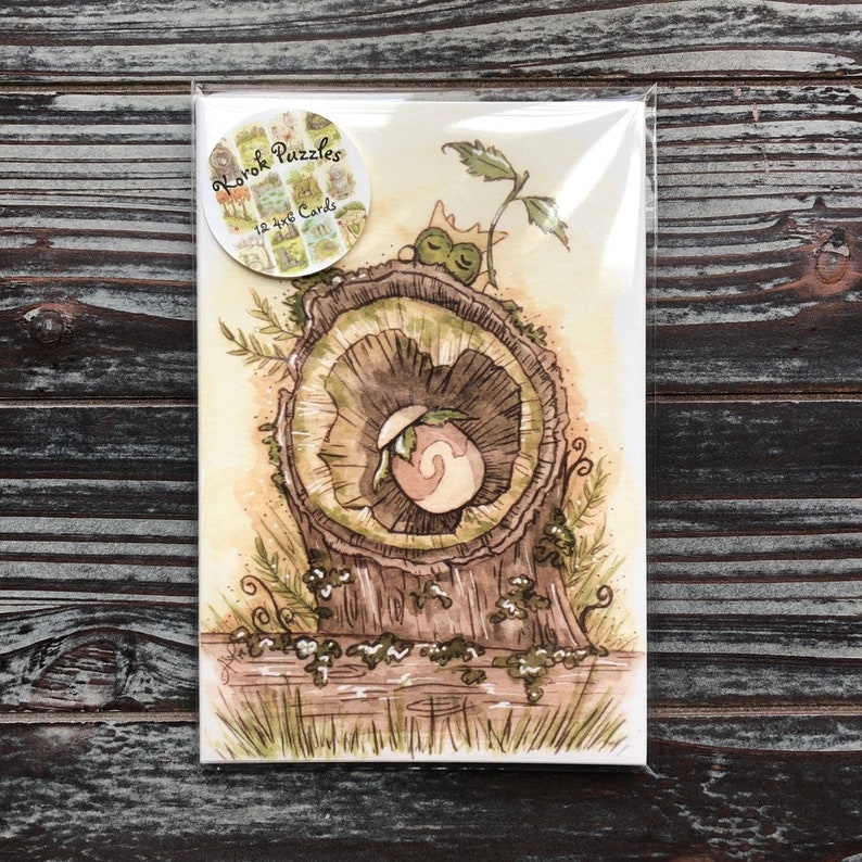 Op de afbeelding: Een pakket van 12 wenskaarten met een aquarel illustratie van een boomstronk en een wezen. De kaarten zitten in een doorzichtige plastic hoes. Het pakket heeft een ronde sticker met de tekst "Korok Puzzles".