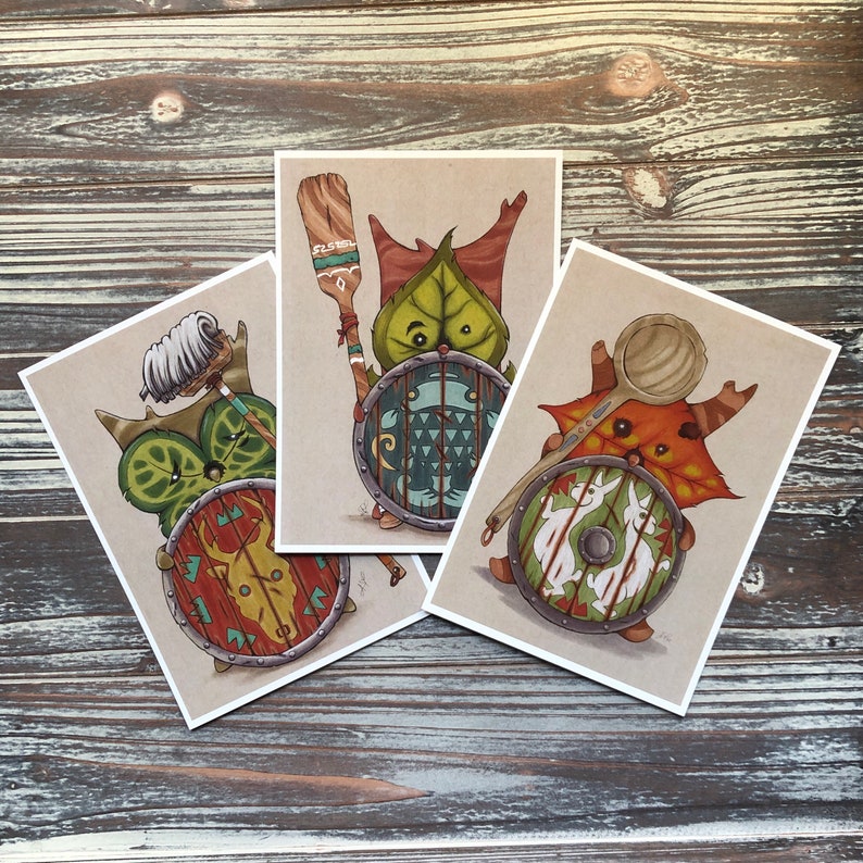 Puede incluir: Tres tarjetas ilustradas con criaturas fant&aacute;sticas con escudos. La primera tarjeta presenta una criatura verde con cabeza en forma de hoja sosteniendo un escudo con un dise&ntilde;o verde, azul y blanco. La segunda tarjeta presenta una criatura marr&oacute;n con un escudo con un dise&ntilde;o rojo, blanco y negro. La tercera tarjeta presenta una criatura marr&oacute;n con un escudo con un dise&ntilde;o blanco, negro y marr&oacute;n.