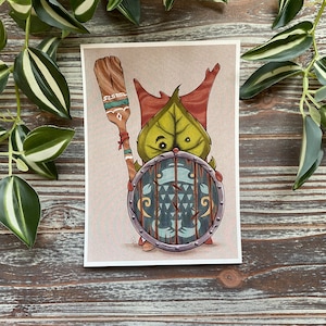 Puede incluir: Una ilustraci&oacute;n de dibujos animados de una criatura de hoja verde sosteniendo un escudo y una paleta de madera. La criatura tiene acentos rojos y marrones y un escudo azul y blanco con un patr&oacute;n geom&eacute;trico.