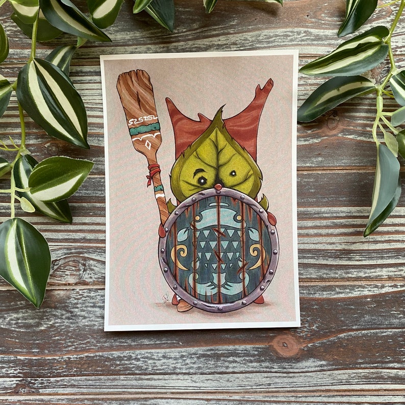 Puede incluir: Una ilustraci&oacute;n de dibujos animados de una criatura de hoja verde sosteniendo un escudo y una paleta de madera. La criatura tiene acentos rojos y marrones y un escudo azul y blanco con un patr&oacute;n geom&eacute;trico.