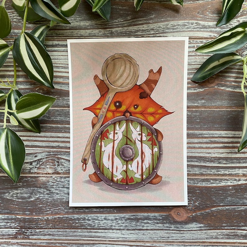 Puede incluir: Una ilustraci&oacute;n caprichosa de una criatura del bosque con un escudo y una cuchara de madera. La criatura se representa como una hoja marr&oacute;n y naranja con una cara y cuernos. El escudo est&aacute; decorado con dos conejos blancos y acentos rojos y verdes.