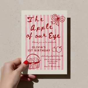 Könnte beinhalten: Eine rechteckige Einladungskarte mit hellrosa vertikal gestreiftem Hintergrund sowie rotem Text und Illustrationen. Der Text lautet: The Apple of our Eye, Please join us to celebrate, OLIVIA'S 1ST BIRTHDAY, Saturday September 10th, 3PM AT OLIVIA'S HOUSE, 129 GALA LANE, SAN DIEGO, rsvp to Olivia's mom. Enthält eine rote Schleife, zwei Äpfel und einen Apfelkorb.