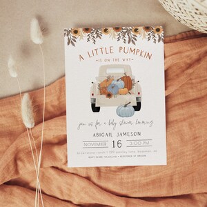 Pu&ograve; includere: Invito per baby shower con un'illustrazione di un camioncino vintage che trasporta zucche. Il testo recita "A Little Pumpkin is on the Way" con i dettagli dell'evento. Il design presenta girasoli e un tema rustico.