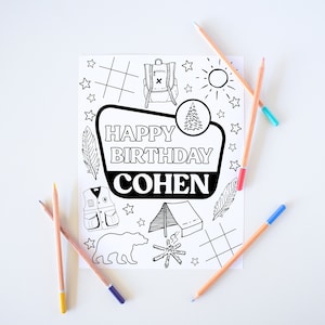 May include: A black and white printable coloring page with a camping theme. The page features a sign that says "Happy Birthday Cohen" and includes images of a tent, a campfire, a bear, a backpack, a tree, and stars.