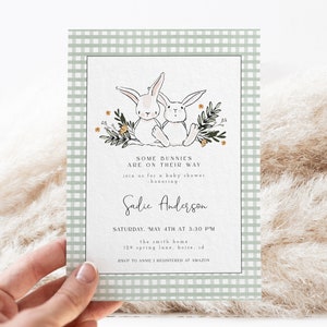 May include: A green and white gingham baby shower invitation with two white bunnies holding carrots. The text reads "Some bunnies are on their way. Join us for a baby shower honoring Sadie Anderson. Saturday, May 4th at 3:30 PM. The Smith Home, 129 Spring Lane, Boise, ID. RSVP to Anne. Registered at Amazon."