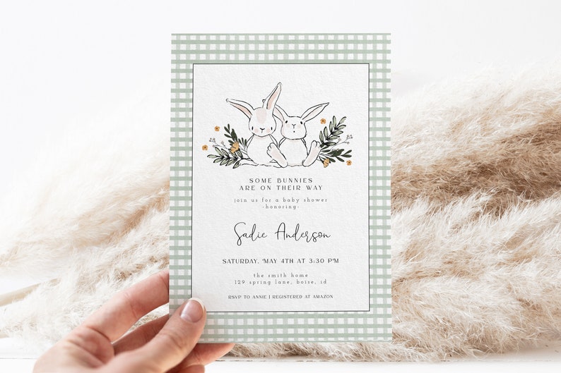 May include: A green and white gingham baby shower invitation with two white bunnies holding carrots. The text reads "Some bunnies are on their way. Join us for a baby shower honoring Sadie Anderson. Saturday, May 4th at 3:30 PM. The Smith Home, 129 Spring Lane, Boise, ID. RSVP to Anne. Registered at Amazon."