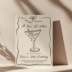 Puede incluir: Una tarjeta de invitación beige con una ilustración verde de una copa de martini y el texto "A tini bit older." La tarjeta también incluye el texto "Join us to celebrate Olivia's 30th Birthday" y detalles sobre el evento: "Saturday, July 12th at 7pm | The Martini Ranch Downtown, Boise | RSVP to Lauren."