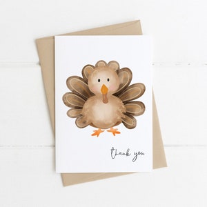 K&ouml;nnte beinhalten: Eine wei&szlig;e Gru&szlig;karte mit einer Aquarellillustration einer Truthahn. Der Truthahn ist braun, beige und orange, mit einem F&auml;cher aus Federn. Die Worte "thank you" sind in einer Schriftart unter dem Truthahn geschrieben. Die Karte liegt auf einem braunen Umschlag.