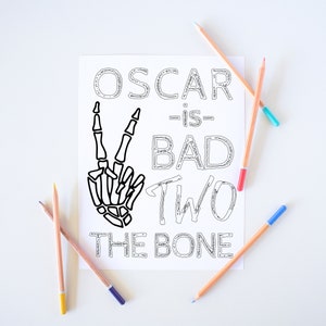 May include: A black and white printable coloring page with the text "Oscar is bad two the bone" and a skeleton hand making a peace sign.
