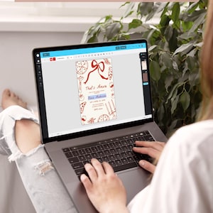 May include: A person using a laptop to view a digital design for a printable invitation. The invitation features a red and white illustration of pizza, wine, and other Italian-themed imagery. The text on the invitation reads "That's Amore" and "Olivia Anderson".