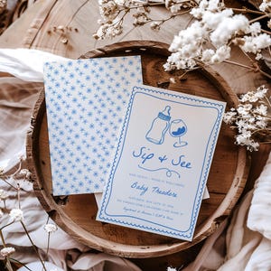May include: A blue and white baby shower invitation with a blue border. The invitation says "Sip & See" and "Baby Theodore". The invitation also includes a drawing of a baby bottle and a glass of wine.