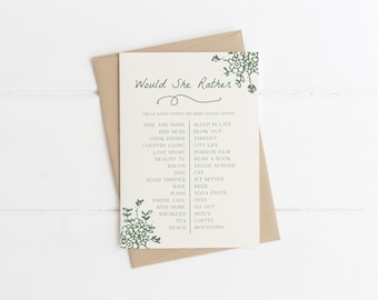 May include: A beige card with the text "Would She Rather" in green script, with a list of choices below. The card is on a brown envelope, with floral designs in the corners. The background is a white wooden surface.