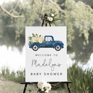 May include: A white sign with a blue pickup truck carrying white flowers. The sign says "Welcome to Madelyn's Baby Shower".
