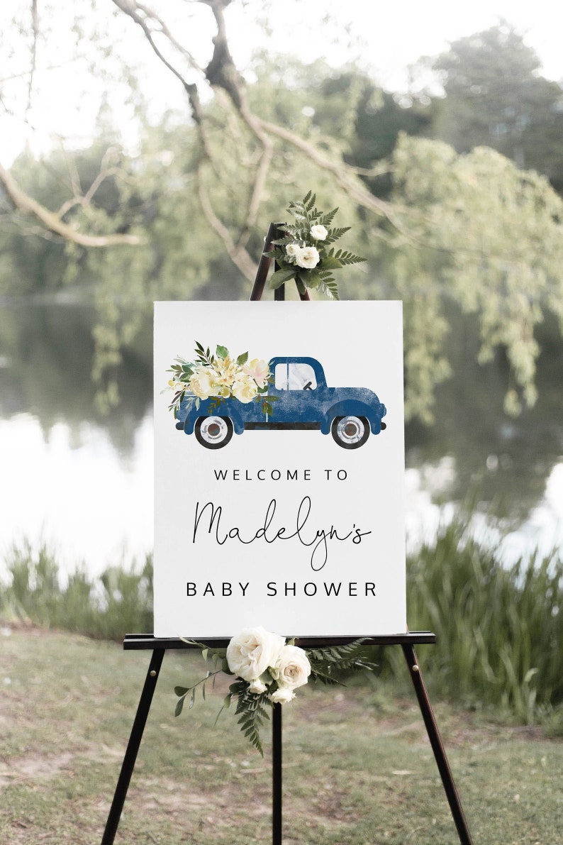 May include: A white sign with a blue pickup truck carrying white flowers. The sign says "Welcome to Madelyn's Baby Shower".