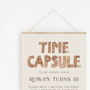 K&ouml;nnte beinhalten: Ein beigefarbenes Schild mit den Worten "TIME CAPSULE" in braunen Holzbuchstaben. Das Schild tr&auml;gt au&szlig;erdem die Aufschrift "Zu &ouml;ffnen, wenn Rowan 18 Jahre alt wird".
