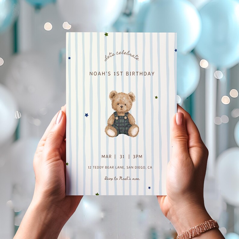 May include: A rectangular birthday invitation card featuring a light blue vertical striped background with small colourful stars. The centre displays a brown teddy bear wearing dark overalls, with text reading Let's celebrate, NOAH'S 1ST BIRTHDAY, MAR 31 3PM, 12 TEDDY BEAR LANE, SAN DIEGO, CA, and Rsvp to Noah's mum.