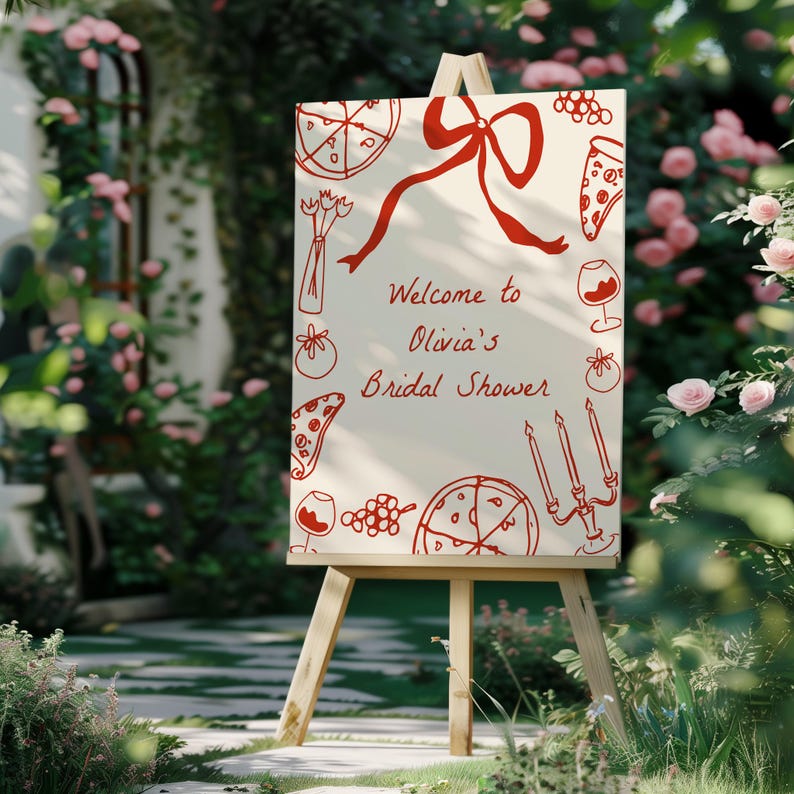 May include: A white sign with red illustrations of pizza, wine glasses, and grapes. The sign reads "Welcome to Olivia's Bridal Shower".