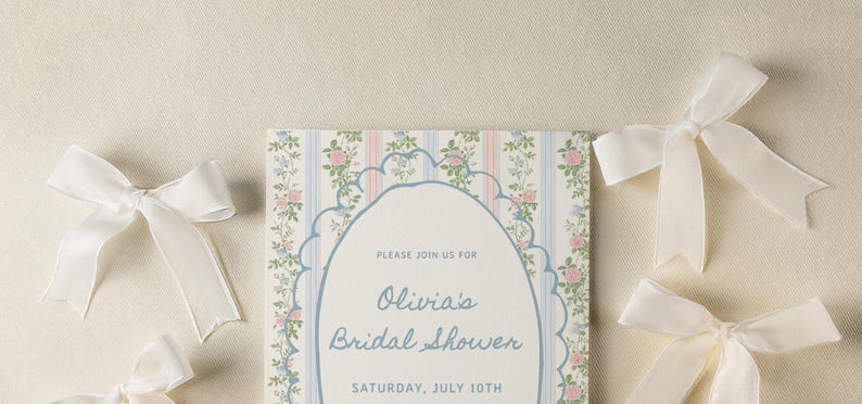 May include: A white card with a floral pattern and blue text that reads "Please join us for Olivia's Bridal Shower Saturday, July 10th".