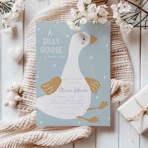 Puede incluir: Una invitación de baby shower azul y blanca con una ilustración de ganso de dibujos animados. El texto dice "A Silly Goose is Almost Loose. It's a Baby Shower Honoring Olivia Johnson. Saturday, April 12th. 3PM at Wildwood Farm, 1 Prairie Lane, Minnetoneka. Registered at Amazon. RSVP Here."