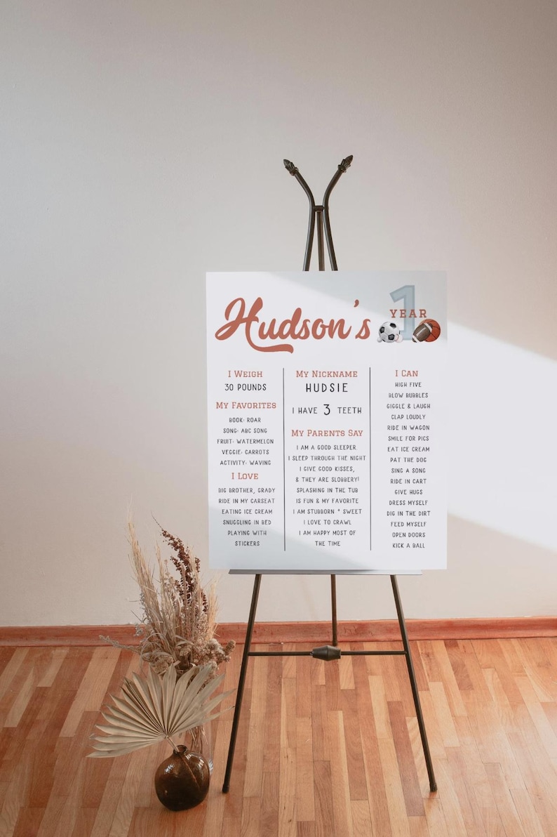 May include: A white poster with a red and white design celebrating a child's first birthday. The poster includes the child's name, Hudson, and details about their first year, including their weight, favorite activities, and things they can do.