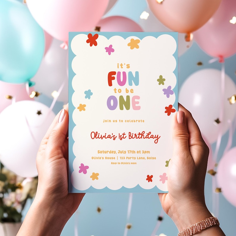 May include: A light blue birthday invitation with the text "it's FUN to be ONE" in colorful letters. The invitation is decorated with colorful flower illustrations and the text "Olivia's 1st Birthday". The invitation is held by two hands.