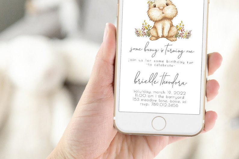 May include: A digital invitation for a first birthday party with a cute cartoon bunny illustration. The invitation says "some bunny is turning one" and includes the name "brielle theodora", the date "saturday, march 19, 2022", the time "11:00 am", the location "the barnyard, 153 meadow lane, boise, id", and the RSVP number "789.012.3456".