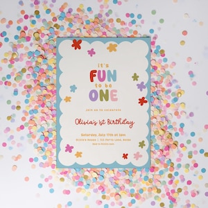 May include: A birthday invitation with a light blue scalloped border, featuring the text "it's FUN to be ONE" in colorful letters. The invitation includes details for Olivia's 1st birthday, surrounded by colorful confetti.