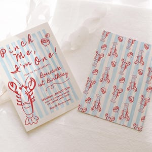 May include: Two invitations with a lobster theme. One features text "Pinch Me, I'm One!" with a lobster illustration and blue stripes. The other has a pattern of lobsters and lemons on blue stripes. The invitations are for Rowan's 1st birthday.